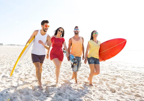Group of friends walking together at the beach and holding surfboards