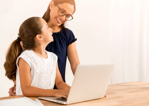 Mother helping her little daughter how to use a computer