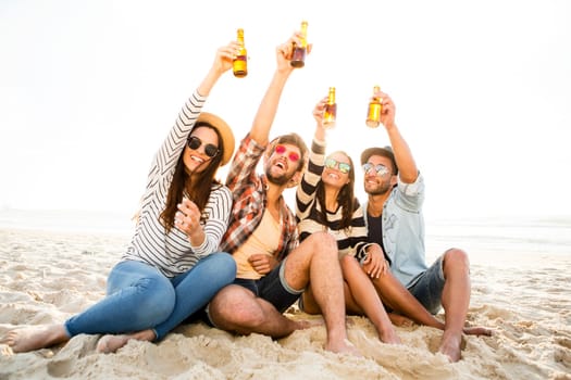 Friends having fun together at the beach and drinking a cold beer