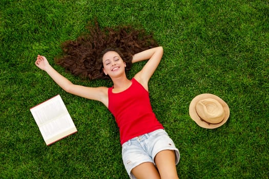 Happy young woman sitting on a blanket with arms stretched