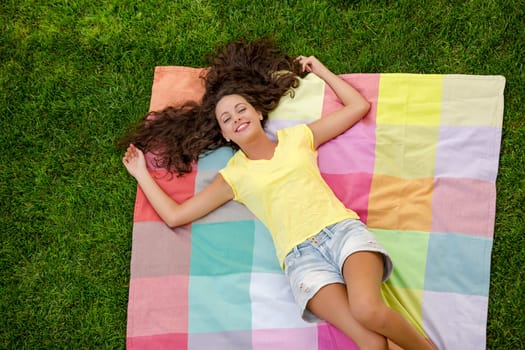 Happy young woman sitting on a blanket with arms stretched