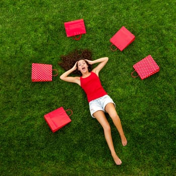 Beautiful and happy young woman lying on the grass surrounded by red gift bags