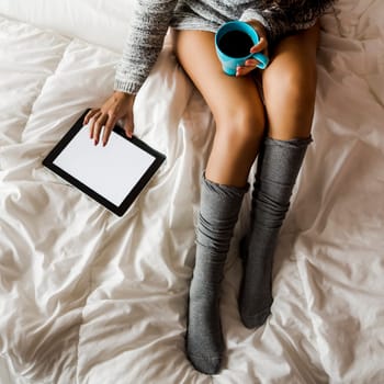 Woman on bed drinking and using a tablet