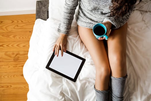 Woman on bed drinking and using a tablet