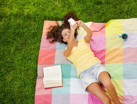 Happy young woman sitting on a blanket with arms stretched