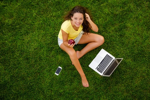 Beautiful young woman lying on the grass and working with a laptop