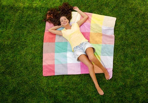 Happy young woman sitting on a blanket with arms stretched