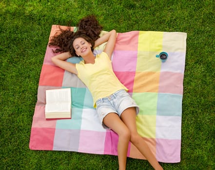 Happy young woman sitting on a blanket with arms stretched