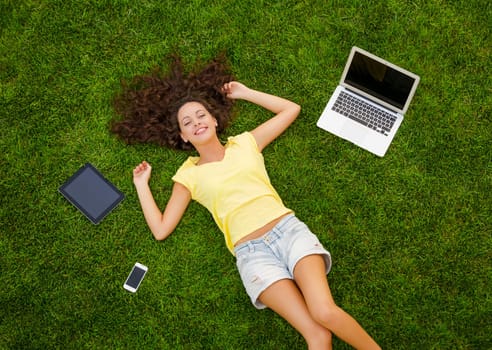 Beautiful young woman lying on the grass and working with a laptop