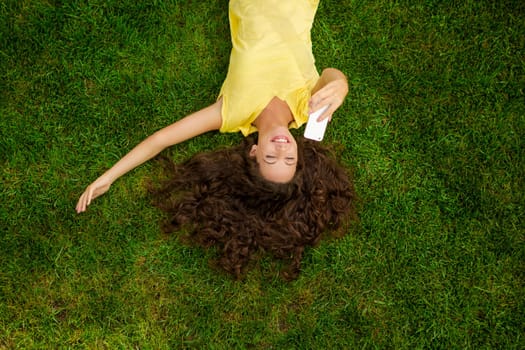 Smiling young woman lying on the grass and making a selfie