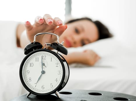 Beautiful young woman waking up with the alarm clock
