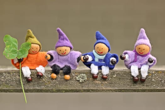 Four small elves with four-leaf clover on a wooden bench