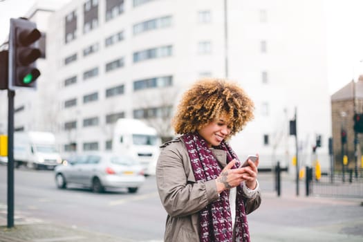 Woman walking in the city. She is holding a smartphone, which she is smiling at.