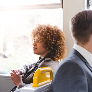 Woman enjoying a sunny train journey. She is sitting next to the window, looking up. There is a man sat behind her.