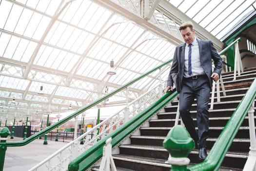 Formal businessman running down the stairs to catch his train at the station. He has a bag on his shoulder.