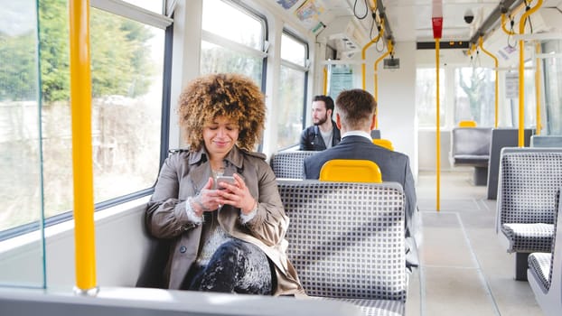 Woman sitting on the train using her smartphone. There are two other passengers out of focus in the background.