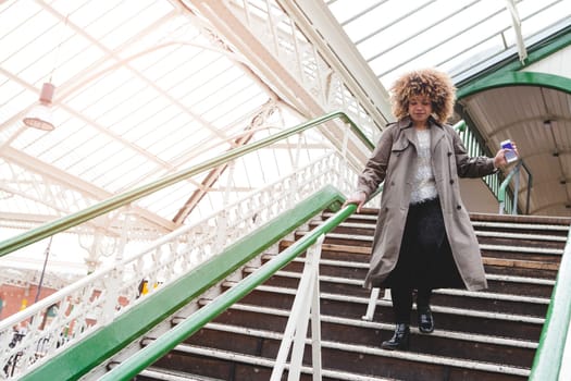 Woman running down the stairs at a train station with her phone in hand. She is late for her train.