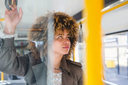 Woman commuting to work on a train. She is standing and holding on to the handle while looking out the window.
