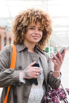 Woman waiting at the train station for her train. She is using her smart phone to check the times.