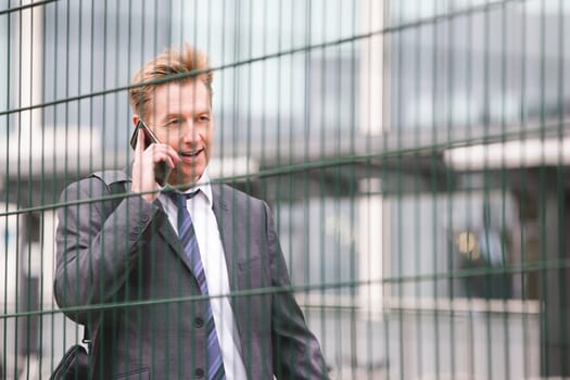 Man in the city talking on the phone. He looks as though he is commuting to work, wearing a formal suit.