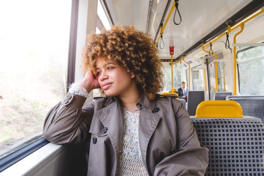 Woman sitting on a train. She has her elbow on the window ledge and is resting her head on her hand, looking out the window.