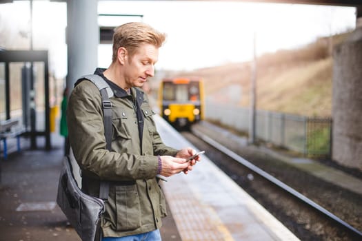 Mature man with a smart phone at a train station. He is about to get on a train that is pulling in.