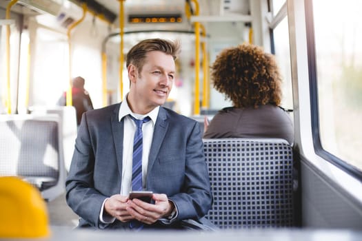 Formal businessman sitting on the train. He is holding a smartphone and looking out the window.
