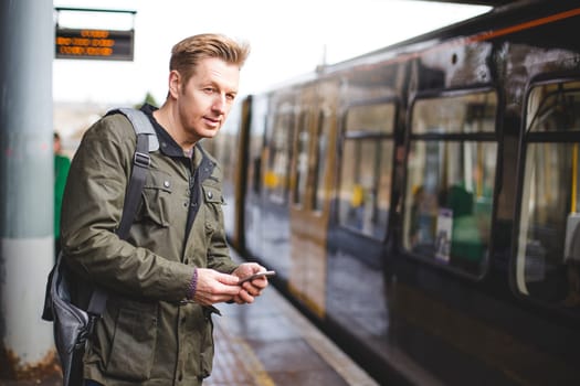 Mature man with a smart phone at a train station. He is about to get on a train that is pulling in.