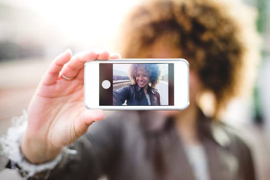 Woman taking a selfie on a smartphone. She is outdoors and the screen of the phone can be seen.