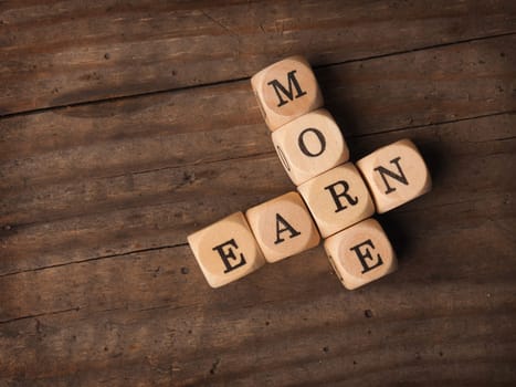 Wooden dices with the words Earn more on a rustic background, financial concept
