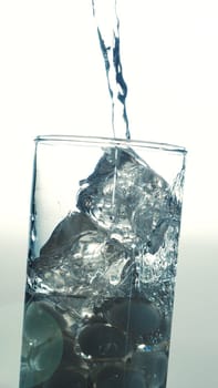 Pouring fresh table water in a glass with ice cubes, vintage film effects with lens flares