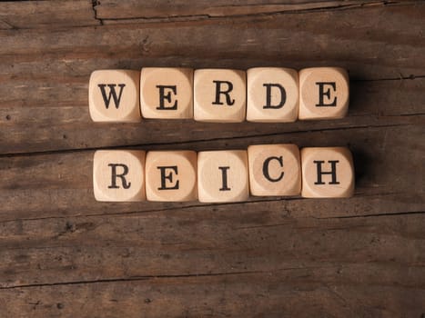 Wooden dices with the German words Get rich on a wooden table