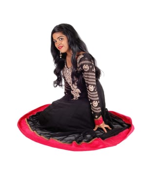 A beautiful Indian woman in a native black dress and long black hair.sitting on the floor, isolated for white background..