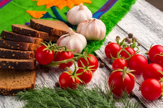 Still life on wooden background: tomatoes, black bread, garlic, fennel, bayberry pepper