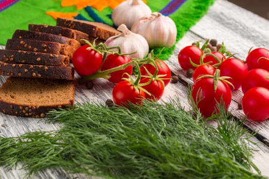 Still life on wooden background: tomatoes, black bread, garlic, fennel, bayberry pepper