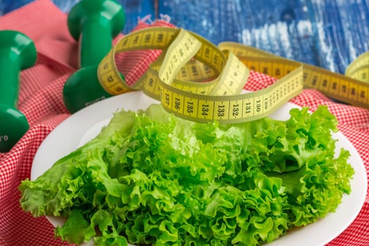 Fitness composition of green lettuce on white plate, weights and ruler
