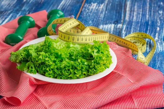 Fitness composition of lettuce on white plate, weights and ruler