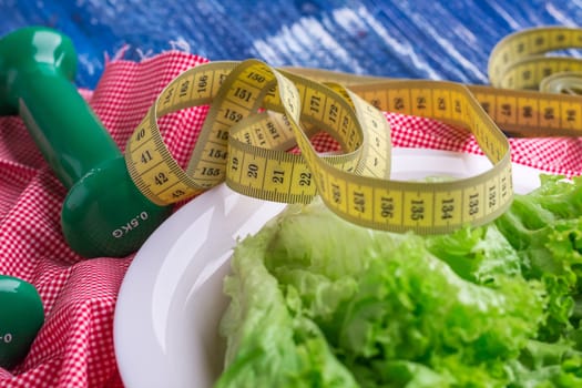 Fitness composition of green lettuce on white plate, weights and ruler