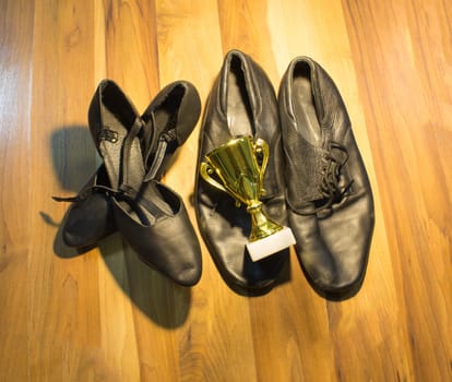 The black dance shoes of the man and woman on wooden floor background and golden cup of winner