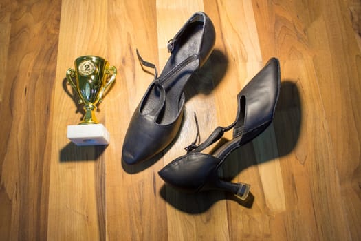 The black dance shoes on wooden floor background and golden cup of winner