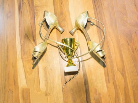 The old latin dance shoes on wooden floor background and golden cup of winner