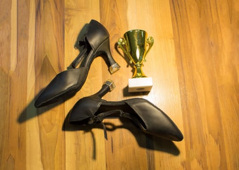 The black dance shoes on wooden floor background and golden cup of winner