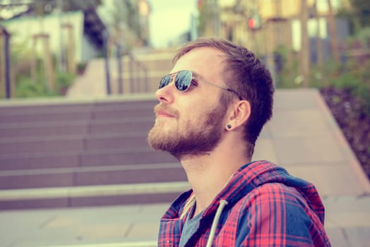 young bearded man with sunglasses in checkered shirt standing on stairs