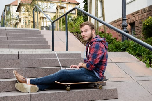 young man in checkered shirt sitting on stairs and using laptop