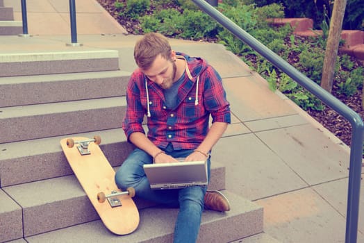 young man in checkered shirt sitting on stairs and using laptop