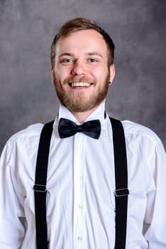 young bearded man in white shirt and bow tie in front of gray background