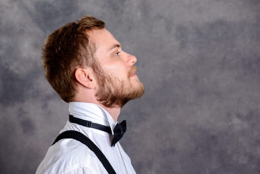 young bearded man in white shirt and bow tie in front of gray background