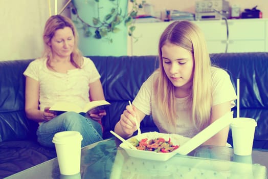 mother reading a book and daughter eating fast food