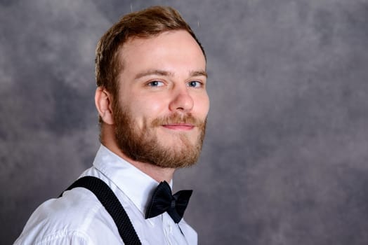 young bearded man in white shirt and bow tie in front of gray background