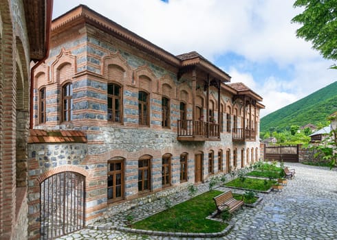 Exterior view of Shaki Khan's Mosque Complex, a historic structure located in Shaki, Azerbaijan. The complex is characterized by its stone walls, wooden balconies, and traditional architecture